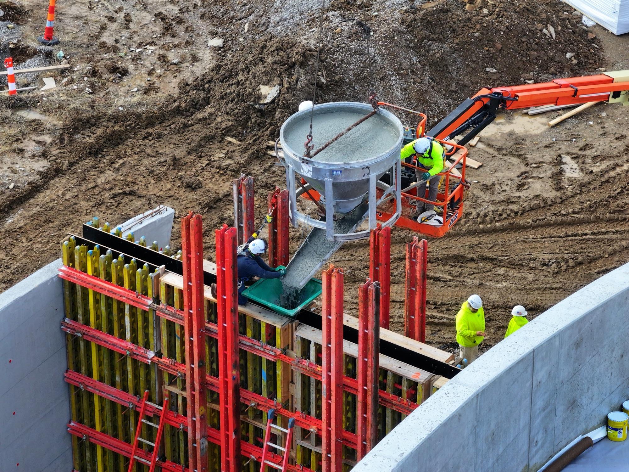 Concrete bucket over red and yellow formwork, boom lift and crew from above