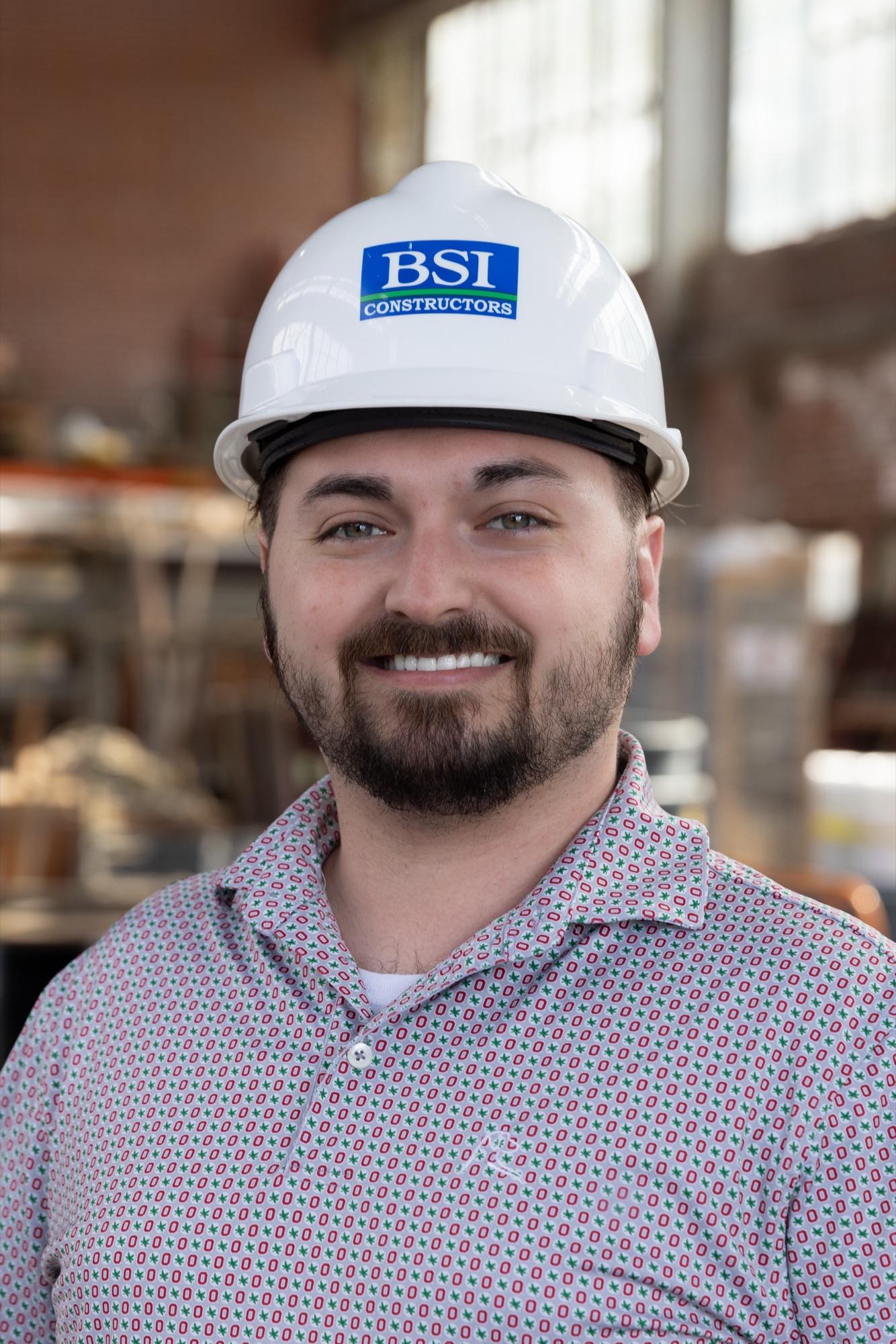 On-site headshot in a hard hat with a jobsite softened behind